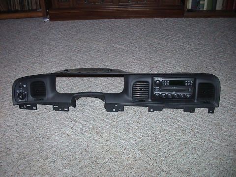 2000 Ford Crown Victoria - A dark gray Ford upper dash bezel removed from the car and laid face-up on beige carpet indoors, complete with headlight and dimmer switche…