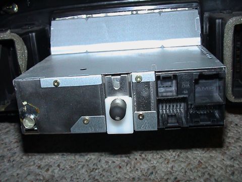 2000 Ford Crown Victoria - Rear view of a removed Ford factory head unit sitting on carpet, showing the bare zinc-plated chassis, a white plastic antenna-lead retaine…