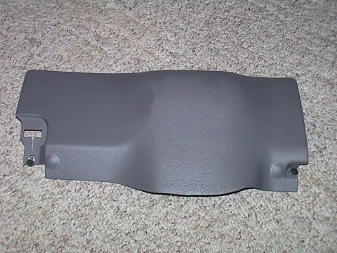 2000 Ford Crown Victoria - A removed grey textured plastic lower dash knee panel lying face-up on beige carpet, with black push-fastener clips still in the mounting h…