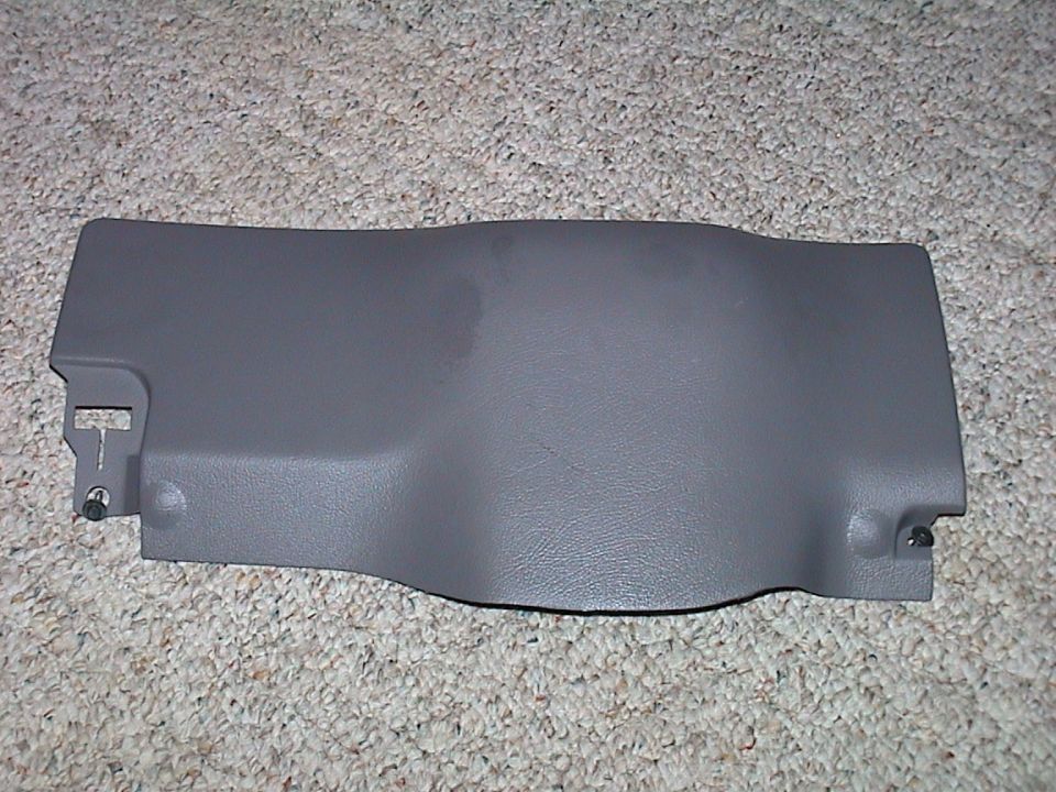 Grey plastic lower dash knee panel removed from a car, lying on beige carpet