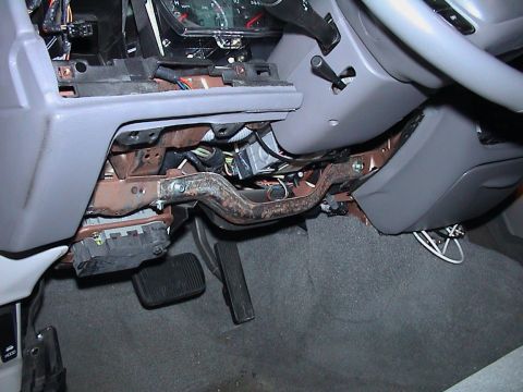 2000 Ford Crown Victoria - Driver's footwell of a gray-interior Ford sedan with the lower dash trim removed, exposing the surface-rusted steel steering column support…