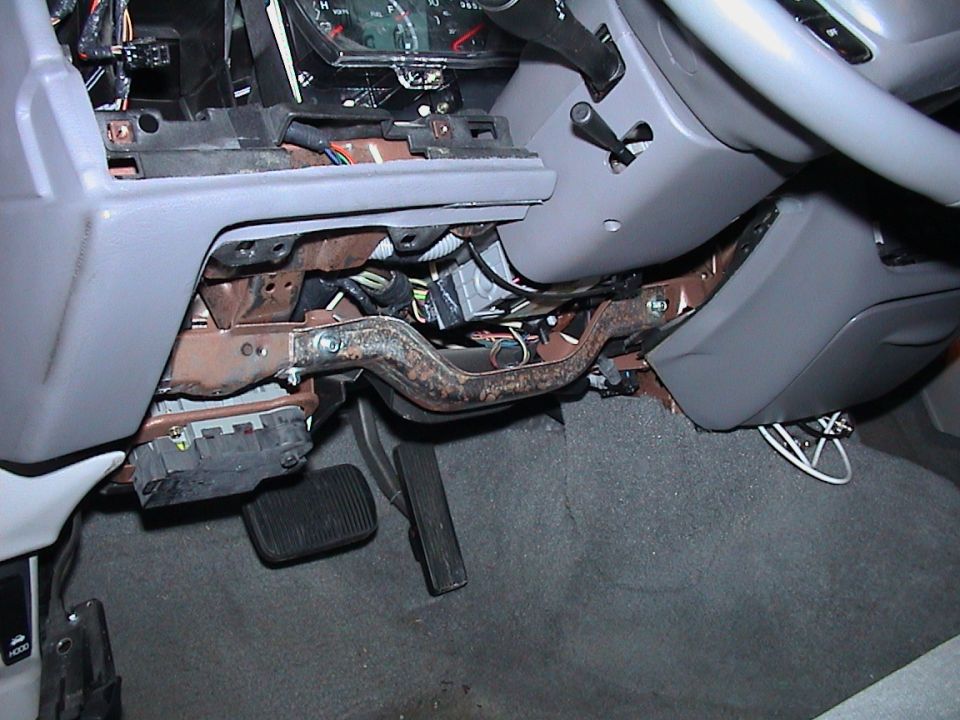 Driver footwell with lower dash removed showing rusty column support and pedals