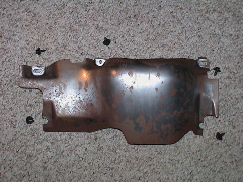2000 Ford Crown Victoria - A stamped-steel under-dash knee bolster or reinforcement bracket removed and laid flat on beige carpet, showing bare metal with widespread…