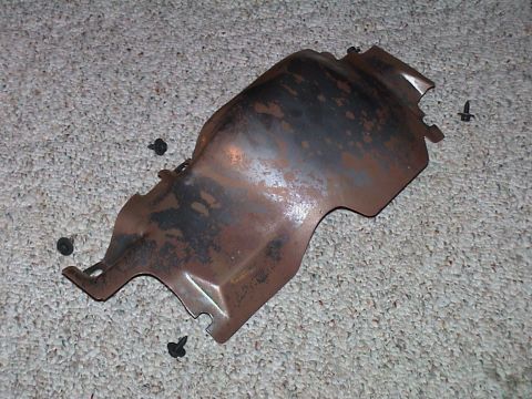 2000 Ford Crown Victoria - A removed stamped-steel under-dash cover or shield lying on beige carpet, its bare surface heavily surface-rusted and mottled brown with cu…