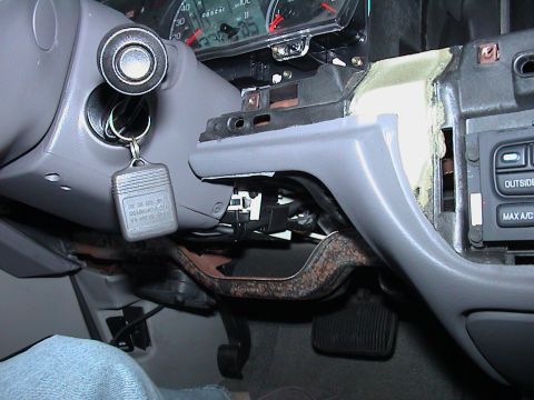 2000 Ford Crown Victoria - Under-dash view on the driver's side of a grey-interior car with the lower trim partly removed, showing exposed wiring, the surface-rusted…
