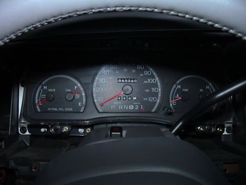 2000 Ford Crown Victoria - Instrument cluster sitting in the dash opening with its trim bezel removed, showing exposed mounting screws and the bare metal frame below.…
