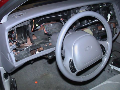 2000 Ford Crown Victoria - Driver's side of a gray Ford sedan interior stripped down to bare dash structure, with the glovebox and center trim gone and harnesses, HVA…