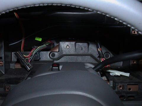 2000 Ford Crown Victoria - Close-up under a dash with the instrument cluster bezel removed, looking past the gray leather-wrapped steering wheel rim at the steering c…
