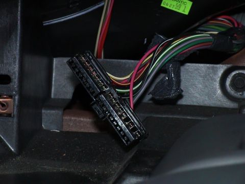 2000 Ford Crown Victoria - Behind-the-dash close-up of a disconnected multi-pin black wiring connector block resting on the dash frame, with color-coded wires and tap…