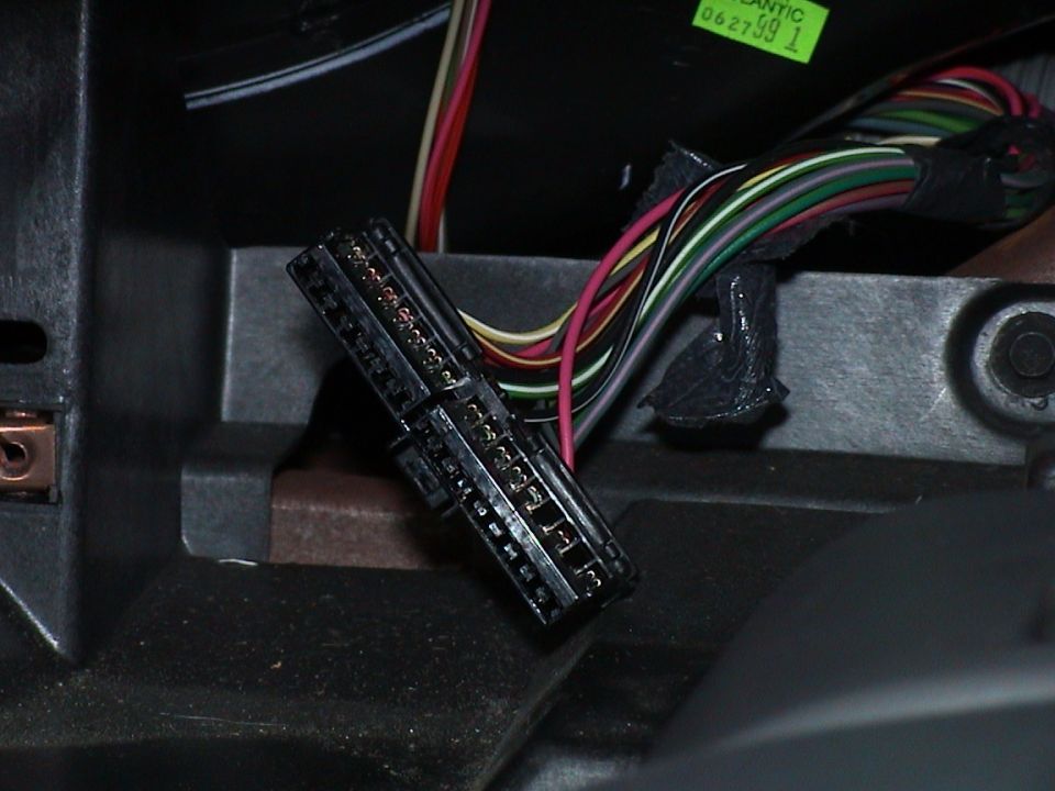 Unplugged multi-pin wiring connector and color-coded harness behind a car dashboard
