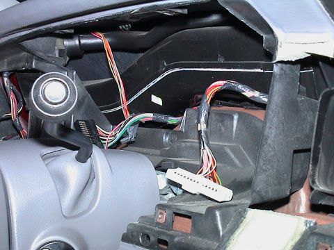 2000 Ford Crown Victoria - Behind the gauge opening of a stripped dash, showing the two unplugged instrument-cluster connectors, a white multi-pin plug hanging on its…
