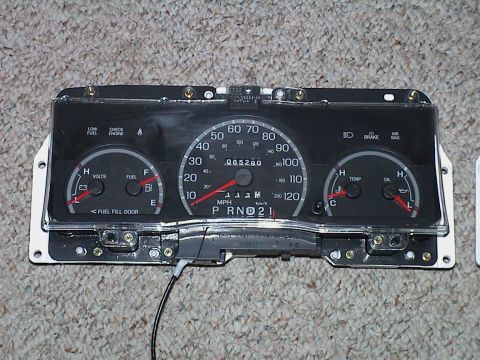 2000 Ford Crown Victoria - A Ford instrument cluster removed from the car and photographed face-up on beige carpet, showing volts and fuel gauges at left, a 120 mph s…