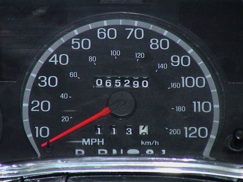 2000 Ford Crown Victoria - Extreme close-up of a black-faced 120 mph analog speedometer with red needle resting at zero, dual MPH and km/h scales, and a mechanical od…