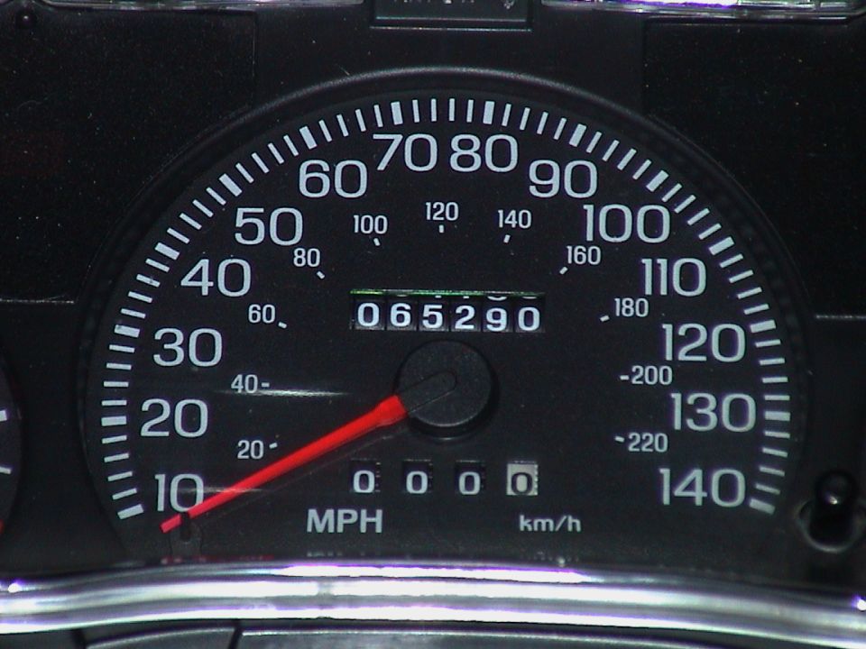 Black speedometer with white numbers and red needle showing 65,290 miles