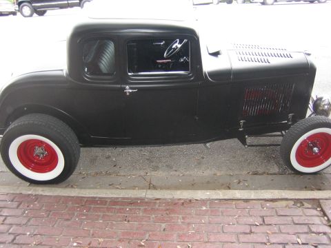 1996 Ford Bronco - A black hot rod coupe with distinctive red wheels and white wall tires is parked curbside.