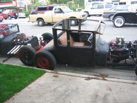 1996 Ford Bronco - Two custom hot rod cars are parked on the street, one black and one red and black.