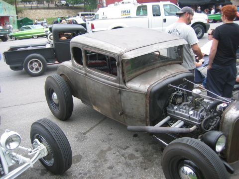 1996 Ford Bronco - A weathered rat rod coupe is parked outdoors, its exposed engine and unique custom build.