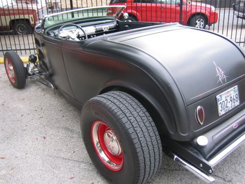 1996 Ford Bronco - A matte black hot rod roadster is parked outdoors, with other vehicles visible behind a fence.