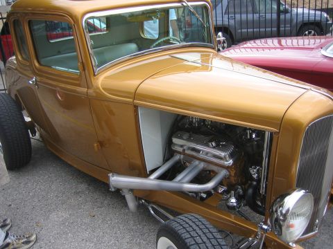 1996 Ford Bronco - A custom gold hot rod coupe is displayed with its engine compartment open, revealing the chrome engine and exhaust headers.