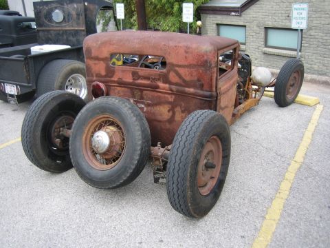 1996 Ford Bronco - A heavily rusted rat rod is parked next to a black pickup truck, with spare tires laid out.