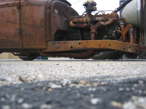 1996 Ford Bronco - A low-angle view of a heavily rusted car chassis and engine, showing exposed mechanical components and frame.