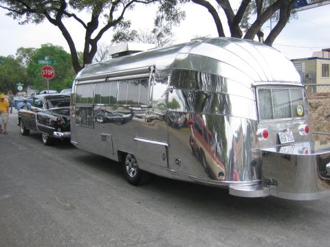 1996 Ford Bronco - A vintage Airstream trailer is pulled by a classic car on a street with trees and a stop sign.
