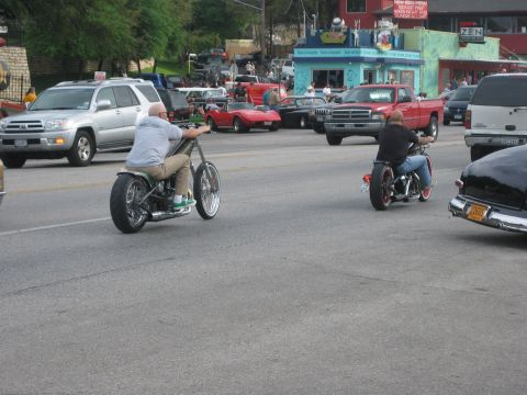1996 Ford Bronco - Two custom motorcycles ride down a street with other vehicles and buildings in the background.