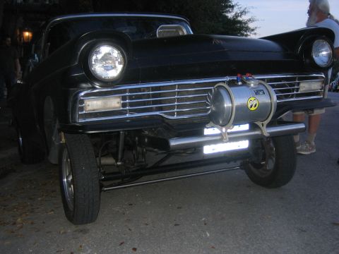 1996 Ford Bronco - Front view of a black 1957 Ford Fairlane hot rod, modified with a hood scoop and a prominent Moon Eyes fuel tank.