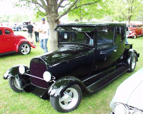 1996 Ford Bronco - A black sedan hot rod is displayed at an outdoor car show with other vehicles in the background.