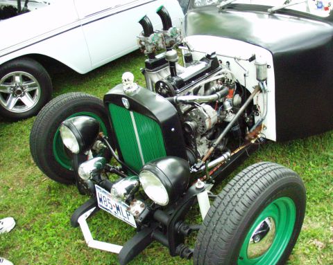 1996 Ford Bronco - A custom hot rod is parked on grass next to another vehicle, its engine and unique front-end details.