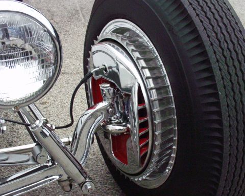 1996 Ford Bronco - Close-up view of a chrome headlight and a wheel red accents and a distinctive chrome hubcap.