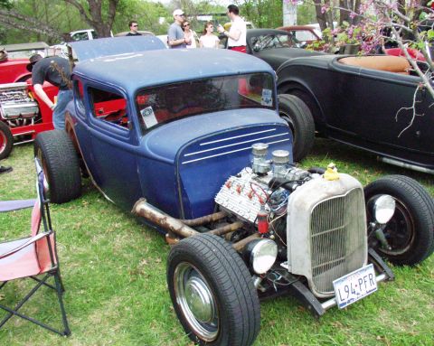 1996 Ford Bronco - Custom hot rod coupe and a black roadster parked on grass at an outdoor car show.