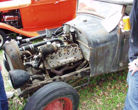 1996 Ford Bronco - A close-up of a vintage hot rod's engine bay and weathered bodywork, with another classic car visible in the background.