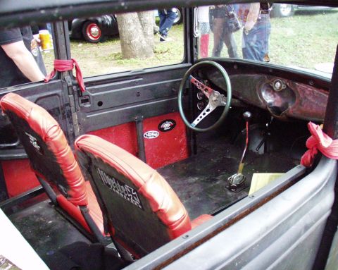 1996 Ford Bronco - The interior of a vintage car features red seats, a custom steering wheel, and exposed metal panels.