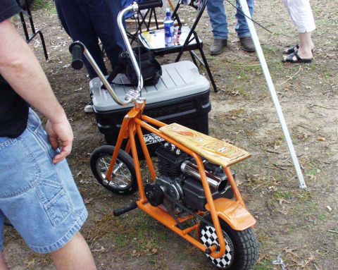 1996 Ford Bronco - A small orange mini bike with a wooden deck sits on the ground, with people in the background.