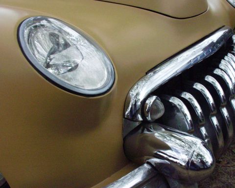 1996 Ford Bronco - Close-up of a gold car's front end, highlighting the chrome grille and headlight detail.