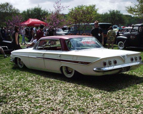 1996 Ford Bronco - A white 1961 Chevrolet Impala with a maroon roof and custom side trim is parked on a grassy field at an outdoor event.