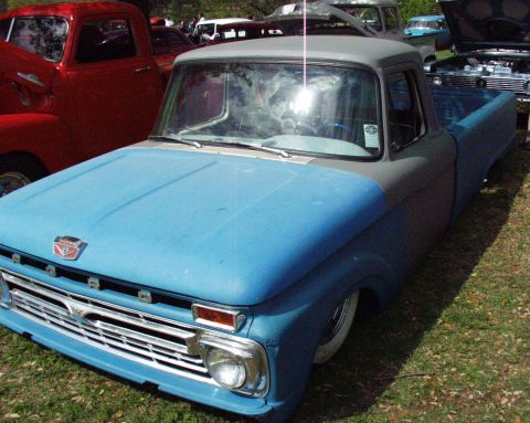 1996 Ford Bronco - A two-tone pickup truck with a lowered stance is parked on grass, grass with other vehicles in the background.