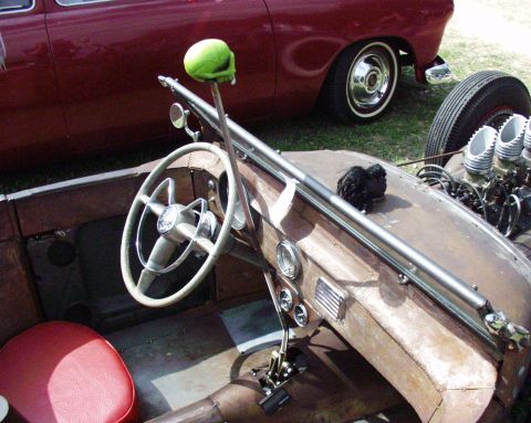 1996 Ford Bronco - Interior view of a custom hot rod a green skull gear shift knob and a red seat, with a vintage car in the background.