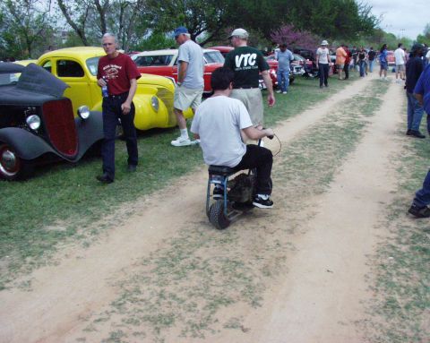 1996 Ford Bronco - A man rides a mini bike down a dirt path at an outdoor event with several classic cars visible.