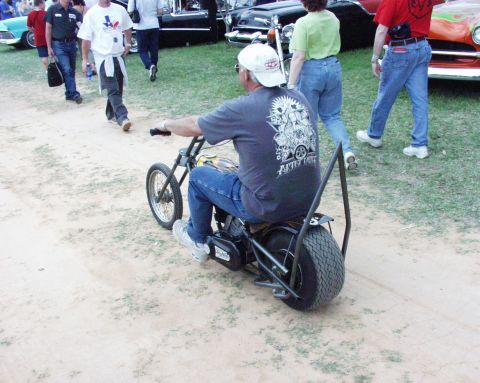 1996 Ford Bronco - A man rides a small motorcycle on a dirt path, with other vehicles and pedestrians visible in the distance.