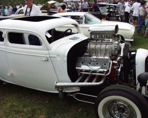 1996 Ford Bronco - A heavily modified white hot rod with a prominent supercharger is displayed at an outdoor event.