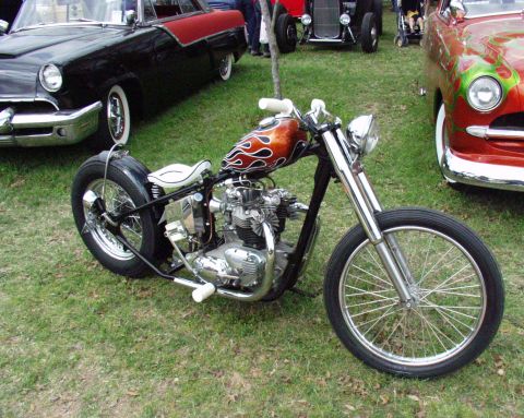 1996 Ford Bronco - Custom chopper motorcycle with flame graphics parked on grass near vintage cars.