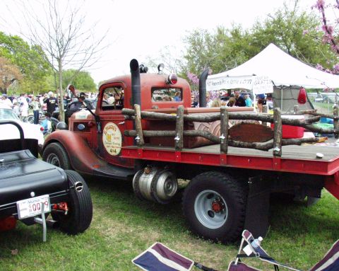 1996 Ford Bronco - A vintage red flatbed truck is parked on grass with other vehicles and tents in the background.