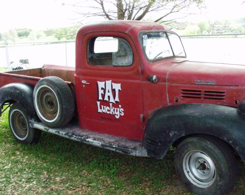 1996 Ford Bronco - A vintage red pickup truck with custom lettering is parked outdoors on a grassy area.