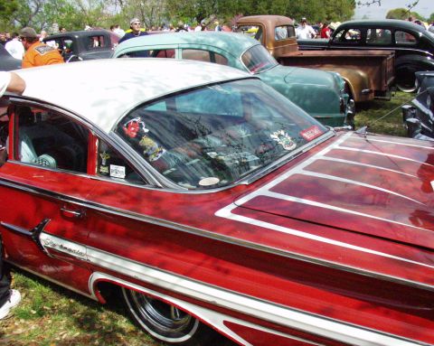 1996 Ford Bronco - A custom red and white car with extensive chrome trim and pinstriping is parked among other vehicles at an outdoor event.