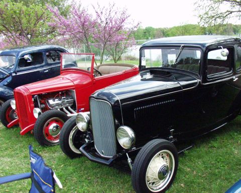 1996 Ford Bronco - Three vintage automobiles, a black coupe, a red roadster, and a blue sedan, are lined up outdoors on a grassy area.