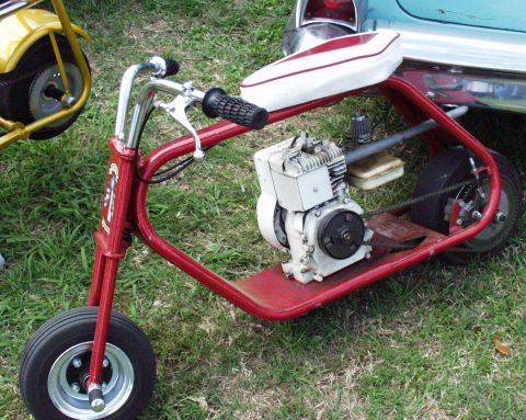 1996 Ford Bronco - A red mini bike with a white seat and visible engine is parked on grass next to another mini bike and a car.