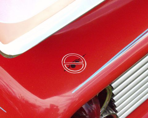 1996 Ford Bronco - A close-up shot focuses on the emblem and chrome grille of a red vehicle, with no clear year identification.