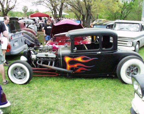 1996 Ford Bronco - A custom hot rod with flame decals is parked on grass at an outdoor car show with other vehicles and tents visible.